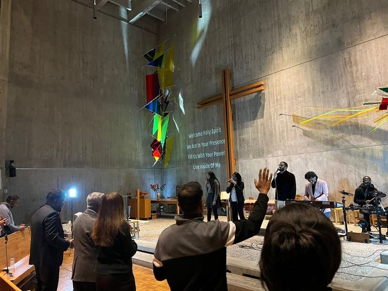 The worship team singing beneath the cross with the words Welcome Holy Spirit projected on the wall