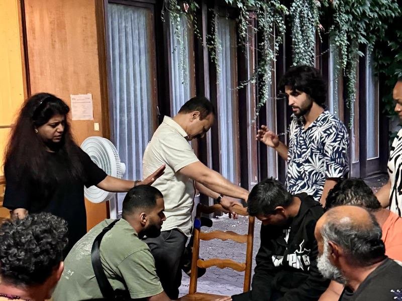 The prayer team laying hands on a young man as the congregation gathers round
