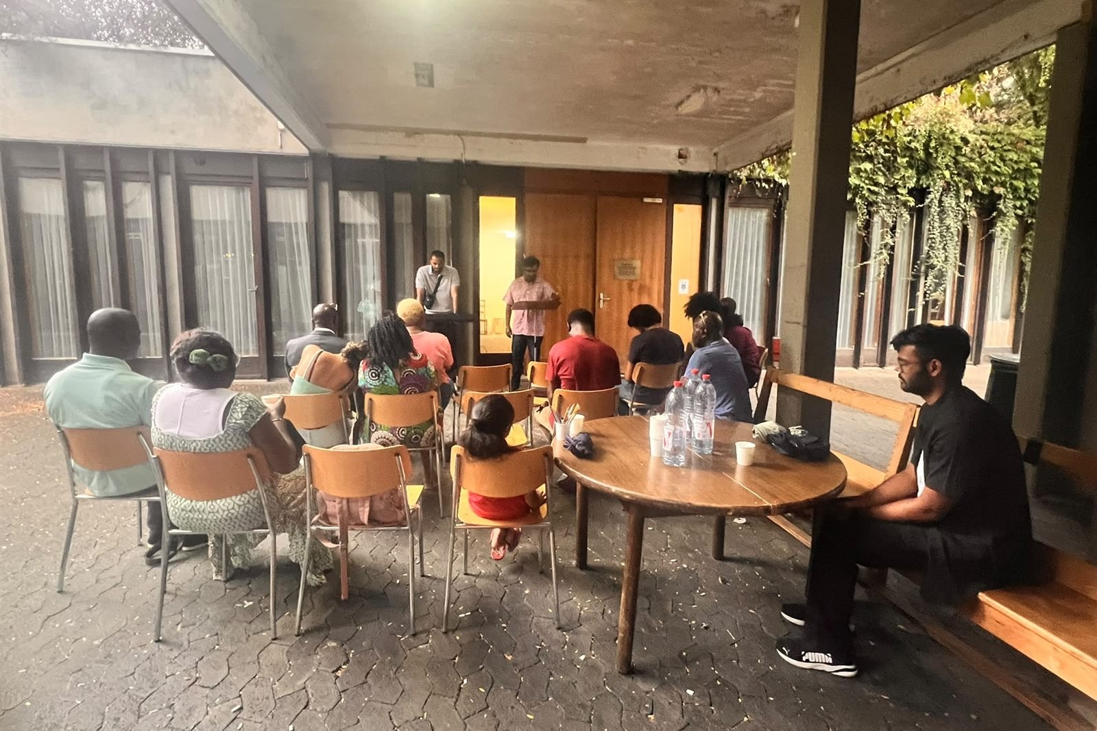 The church gathered on chairs in the covered courtyard at Avenue Wendt 55 on a summer evening