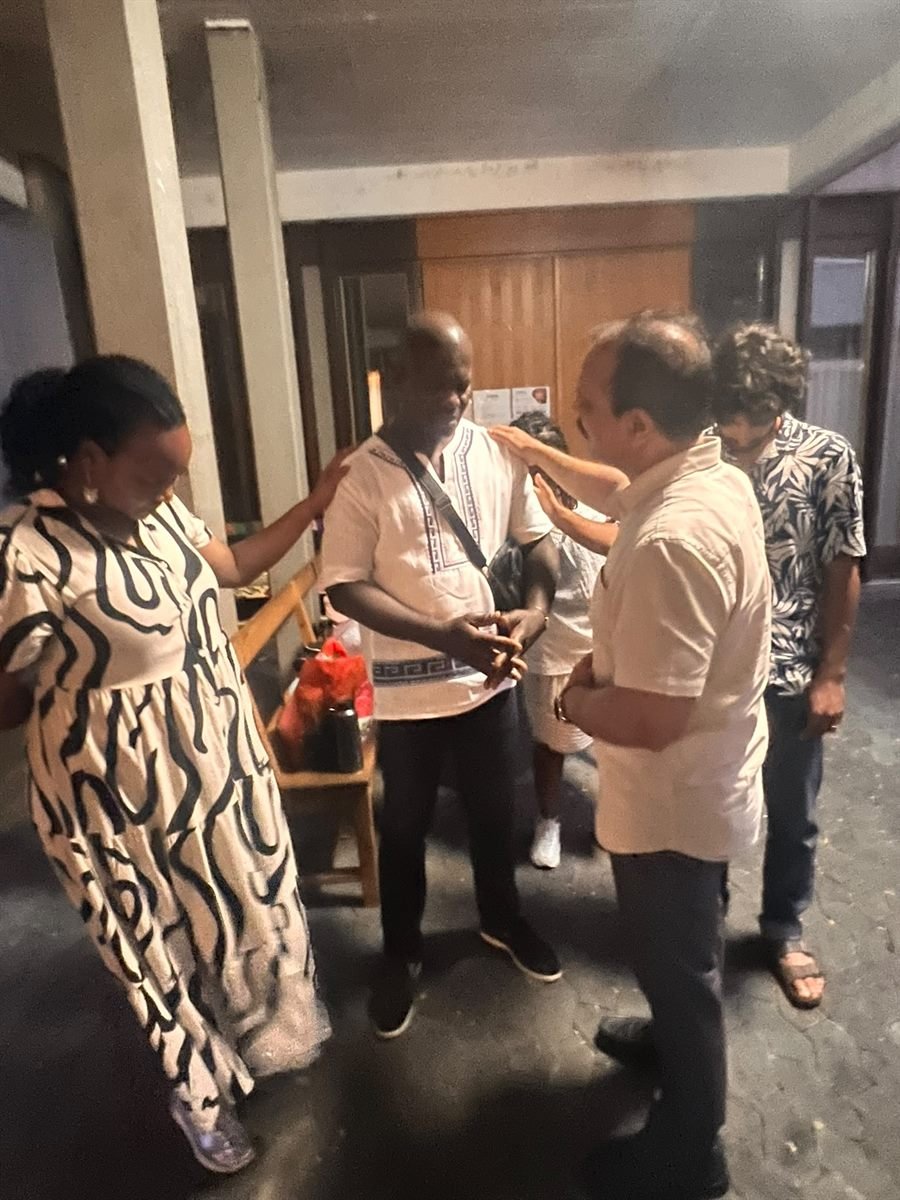Two believers praying over a man with their hands on his shoulders